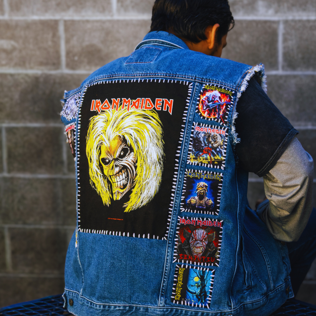 Person wearing a denim vest with Iron Maiden patches against a brick wall.