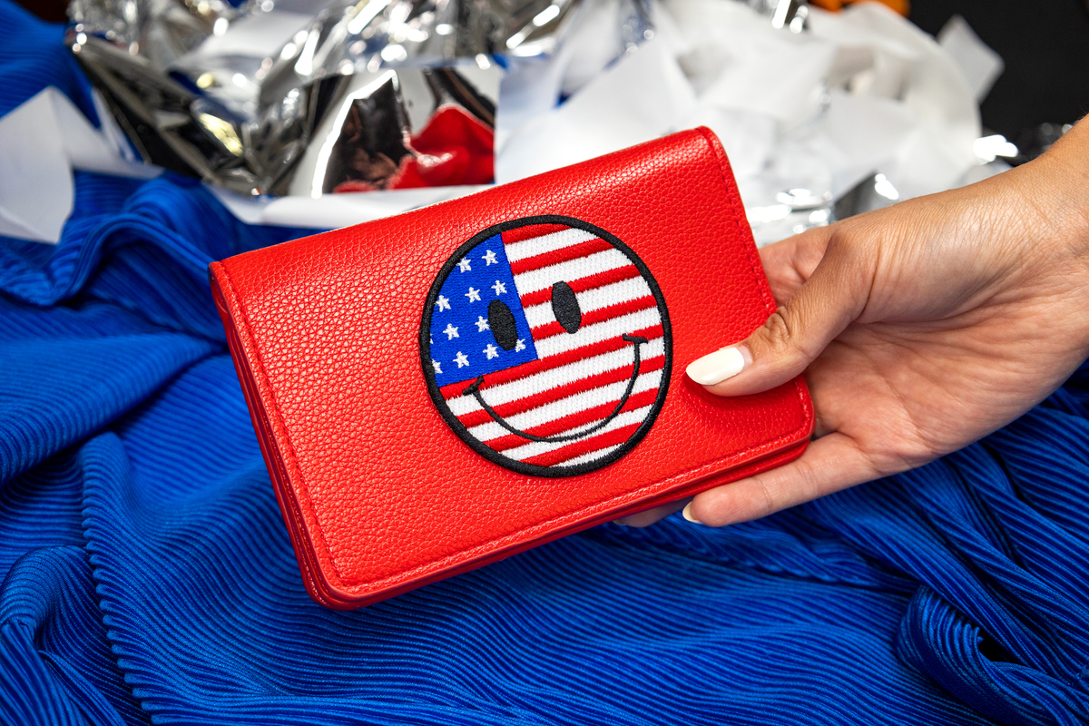 Red wallet with American flag design held by a hand against a blue background