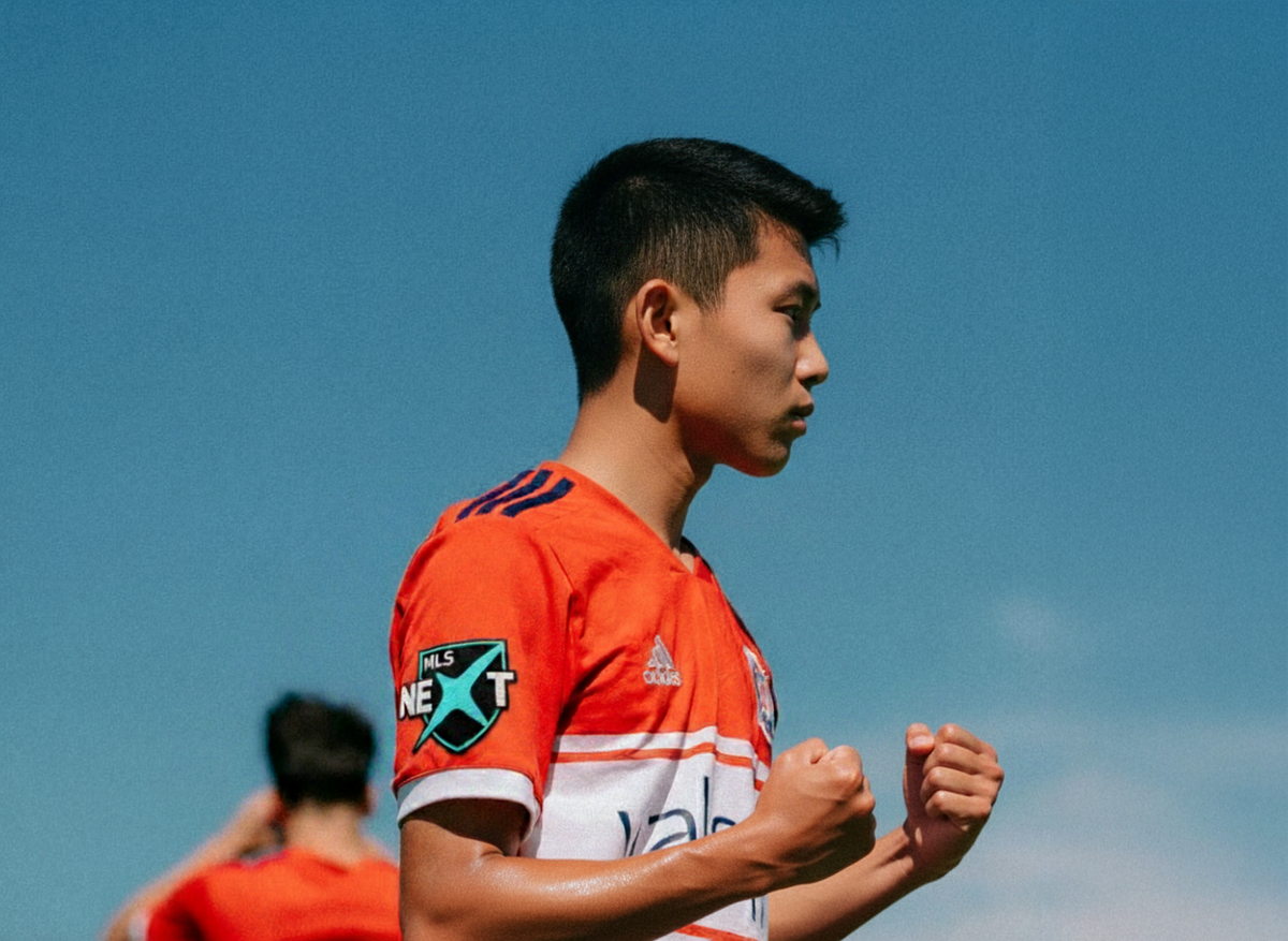 Person wearing an orange sports jersey with a logo against a blue sky