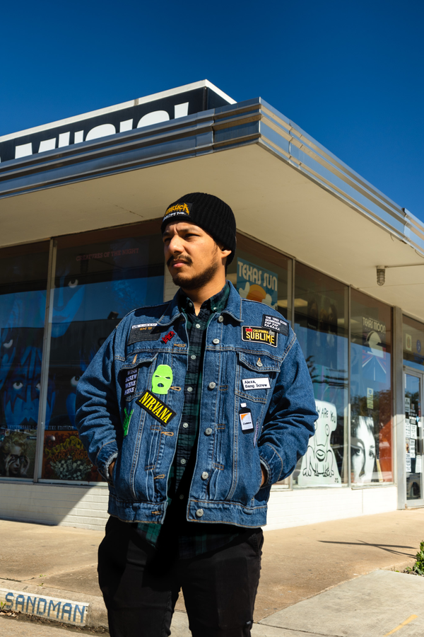 Man wearing a denim jacket with patches in front of a store
